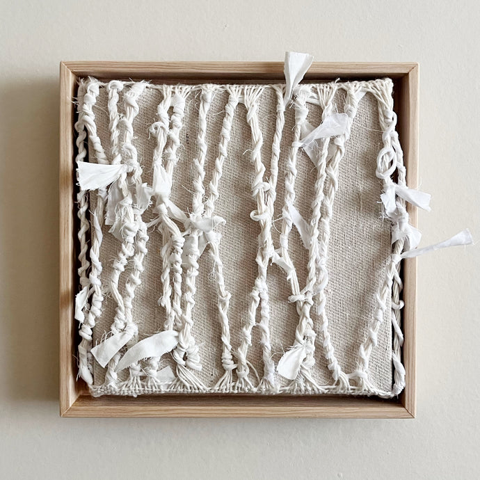 small square textural white weaving floating in a light wood frame