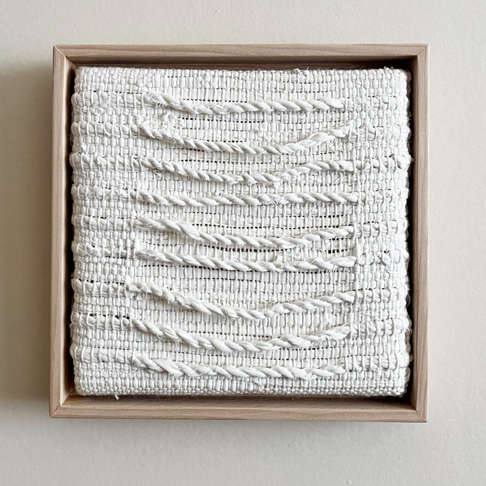 small square textural white weaving floating in a light wood frame