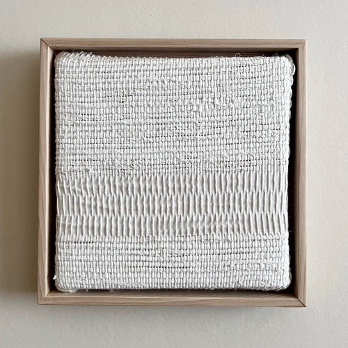 small square textural white weaving floating in a light wood frame