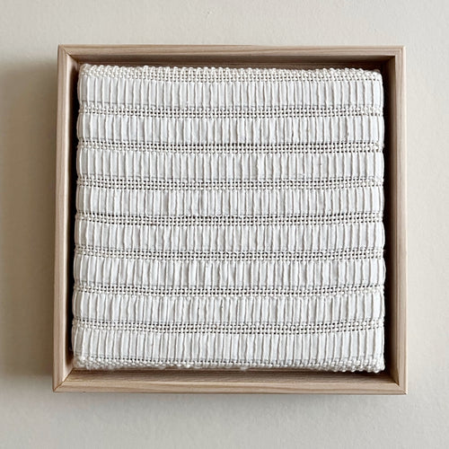 small square textural white weaving floating in a light wood frame