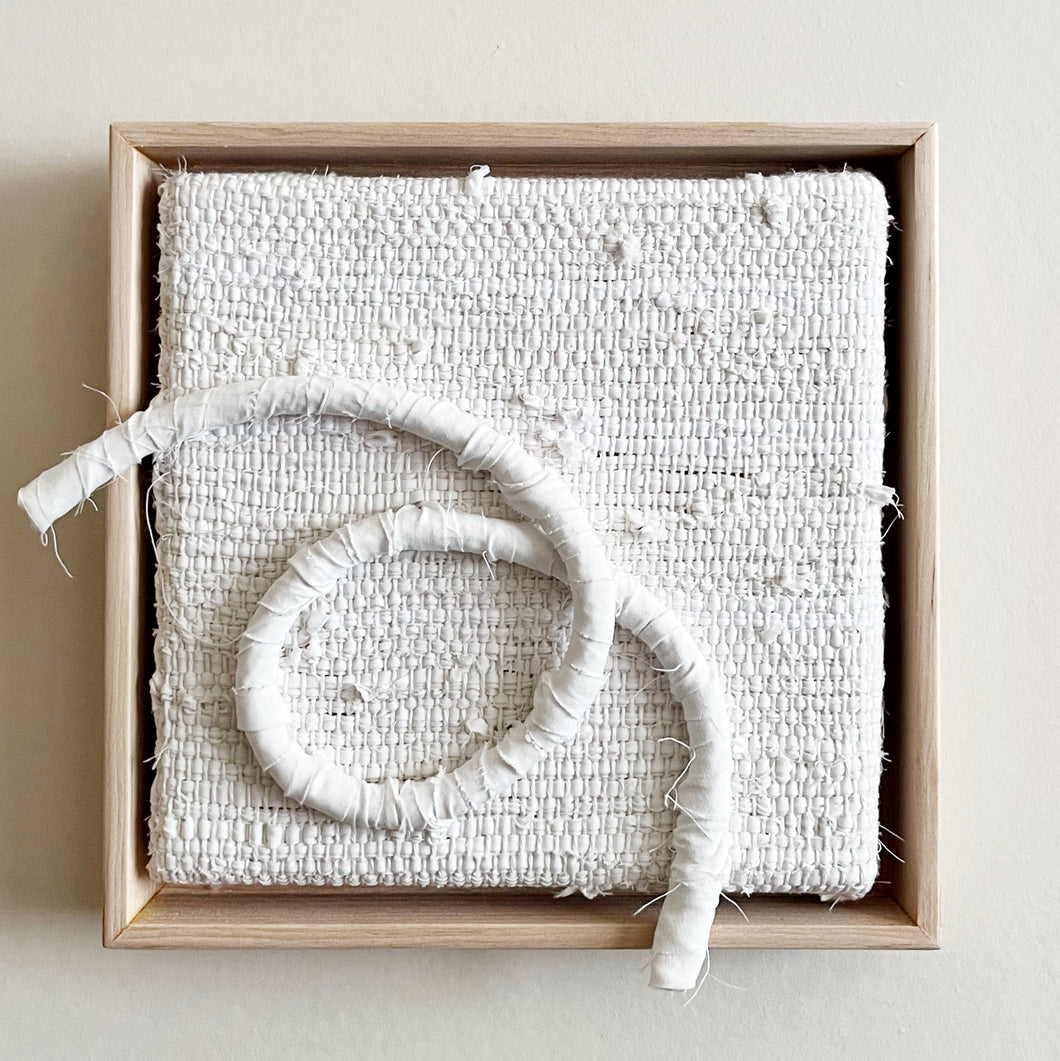 small square textural white weaving floating in a light wood frame