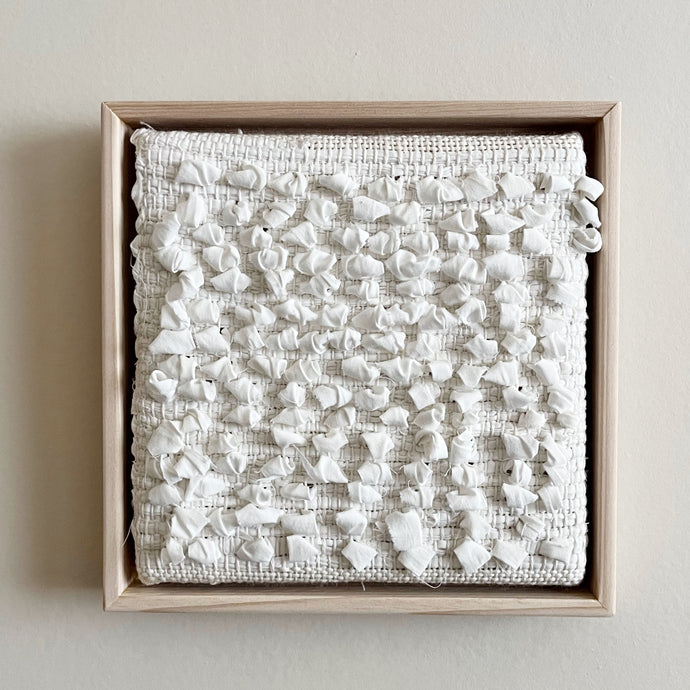 small square textural white weaving floating in a light wood frame