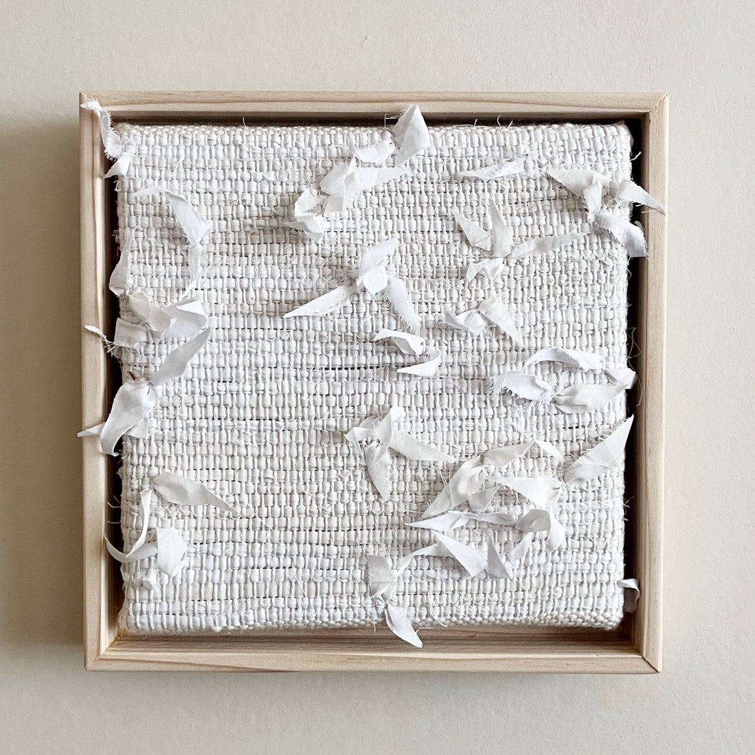 small square textural white weaving floating in a light wood frame