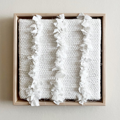 small square textural white weaving floating in a light wood frame