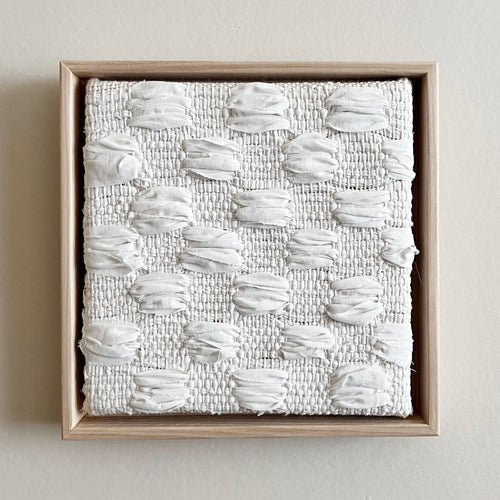 small square textural white weaving floating in a light wood frame