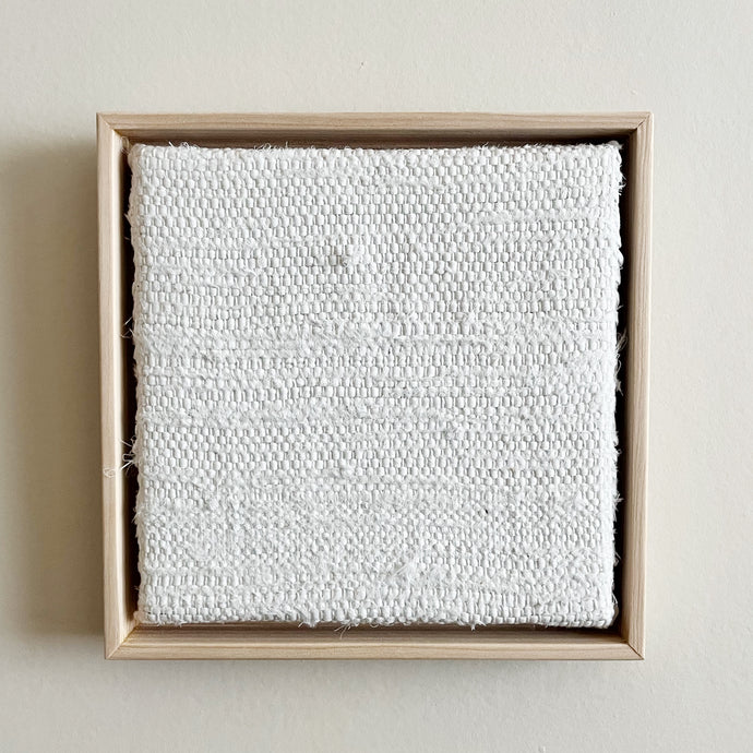 small square textural white weaving floating in a light wood frame