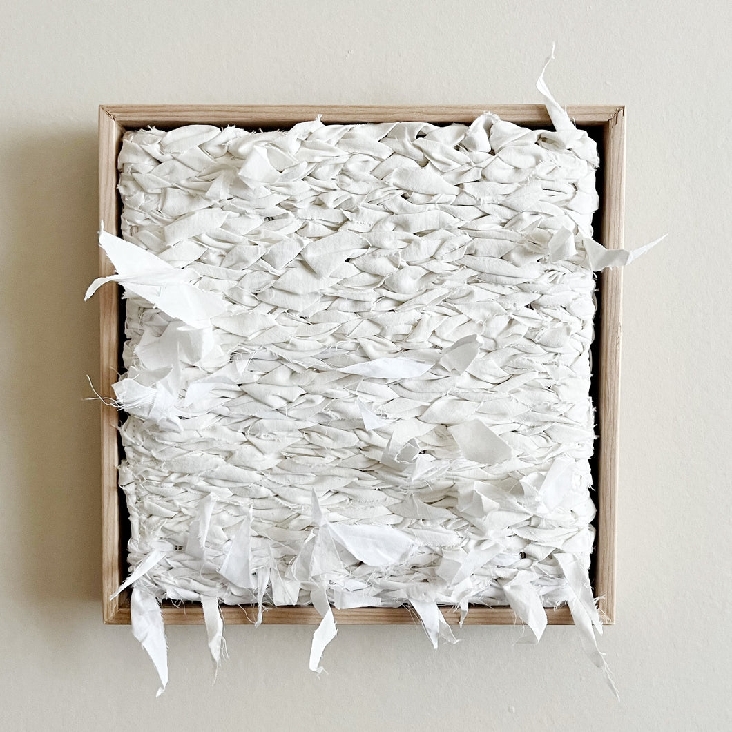 small square textural white weaving floating in a light wood frame