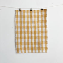 Load image into Gallery viewer, a handwoven white and yellow checked teatowel hangs on a clothesline in front of a white wall
