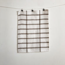Load image into Gallery viewer, a handwoven white and brown teatowel hangs on a clothesline in front of a white wall

