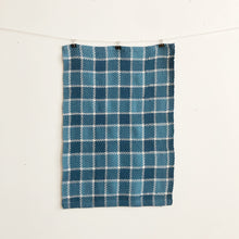 Load image into Gallery viewer, a handwoven blue checked teatowel hangs on a clothesline in front of a white wall
