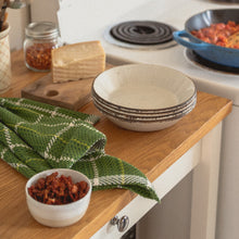 Load image into Gallery viewer, a green teatowel, a stack of white bowls and a block of cheese sit next to a blue pan on the stove filled with red sauce
