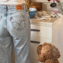 Load image into Gallery viewer, a woman wearing blue jeans stirs cookie dough in a blue bowl on the counter while a shaggy red dog watches attentively
